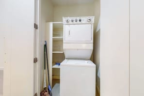 A compact laundry room with a stacked washer and dryer, a broom, and a mop. - La Isla Condominiums #C105 (South Padre Island)