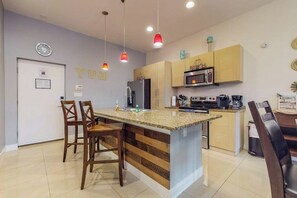 A modern kitchen with a central island, wooden chairs, a microwave, and a coffee machine. - La Isla Condominiums #C105 (South Padre Island)