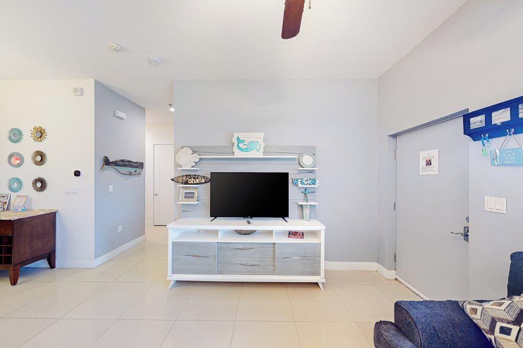 Una sala de estar con un mueble blanco para entretenimiento, un televisor de pantalla plana y un sofá azul.