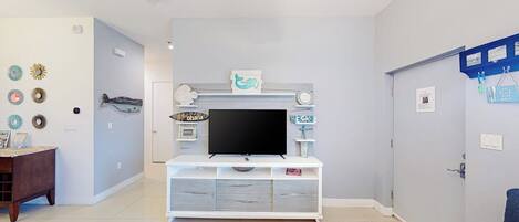 Una sala de estar con un mueble blanco para entretenimiento, un televisor de pantalla plana y un sofá azul.