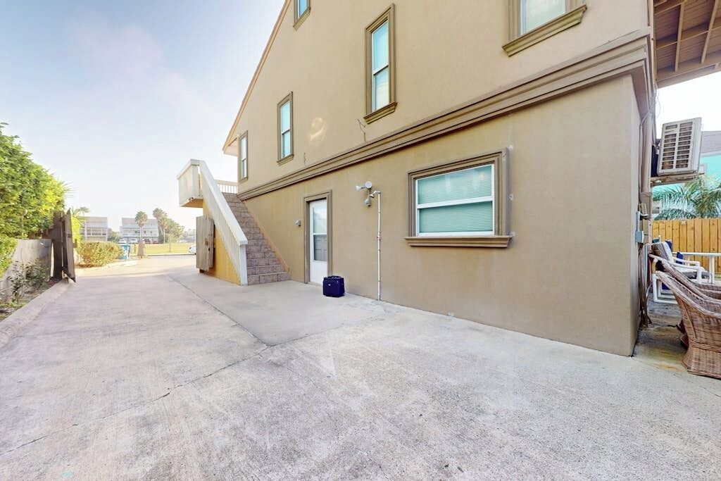 Um prédio residencial com calçada de concreto, escadas que levam à entrada e uma área externa coberta com móveis.
