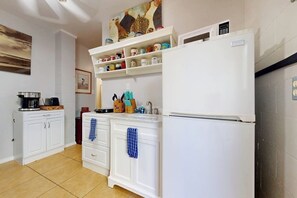 A kitchen with white cabinetry, a refrigerator, and a shelf with various kitchen items. - White Granite at 106 East Huisache (South Padre Island)