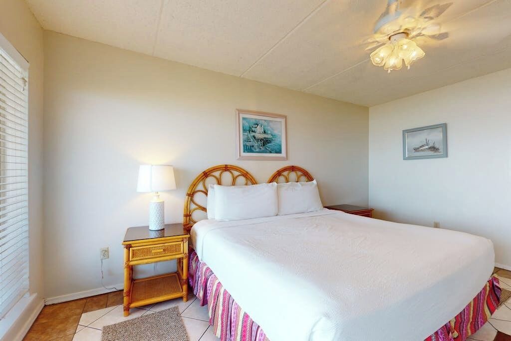A bedroom with a large bed, a bedside table with a lamp, and two framed pictures on the wall.