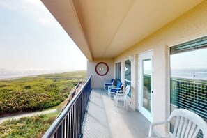 Ein Balkon mit Blick auf den Strand, weiße Stühle und eine Uhr an der Wand.