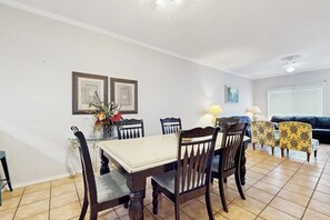 A dining area with a table and chairs, a sofa, and a window with blinds. - Dolphin Condominiums #5 (South Padre Island)