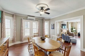 Un coin repas avec une table et des chaises en bois, un ventilateur de plafond et une vue sur un salon comprenant un canapé et un téléviseur.