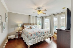 Une chambre à coucher comprenant un lit, une table de chevet, une lampe, un ventilateur de plafond et un téléviseur.