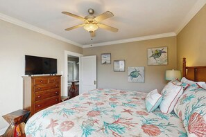 A bedroom with a bed, a ceiling fan, a television, and artwork on the walls. - Salty Toes - Fenced Yard, Steps to the Sand (Galveston)