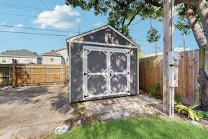 A single-story shed with a gabled roof and a white door. - Salty Toes - Fenced Yard, Steps to the Sand (Galveston)