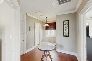 A hallway with a round marble table, white doors, a ceiling vent, and a window with blinds. - Salty Toes - Fenced Yard, Steps to the Sand (Galveston)
