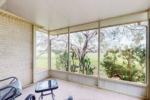A covered patio with a brick wall, a glass door, and a view of a grassy area with trees. - 9 Augusta Casita at SPI Golf Course (Laguna Vista)