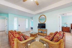 A living room with wicker furniture, a television on a stand, and a mirror on the wall. - 9 Augusta Casita at SPI Golf Course (Laguna Vista)