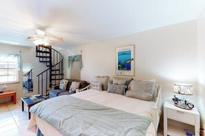 Ein Schlafzimmer mit einem Bett, einem Nachttisch, einem Schreibtisch, einem Sessel, einer Treppe und einem Wandbild.