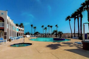 A pool area with multiple swimming pools, lounge chairs, and palm trees. - Long Island Village 790 W Oyster Drive Bungalow (Port Isabel)