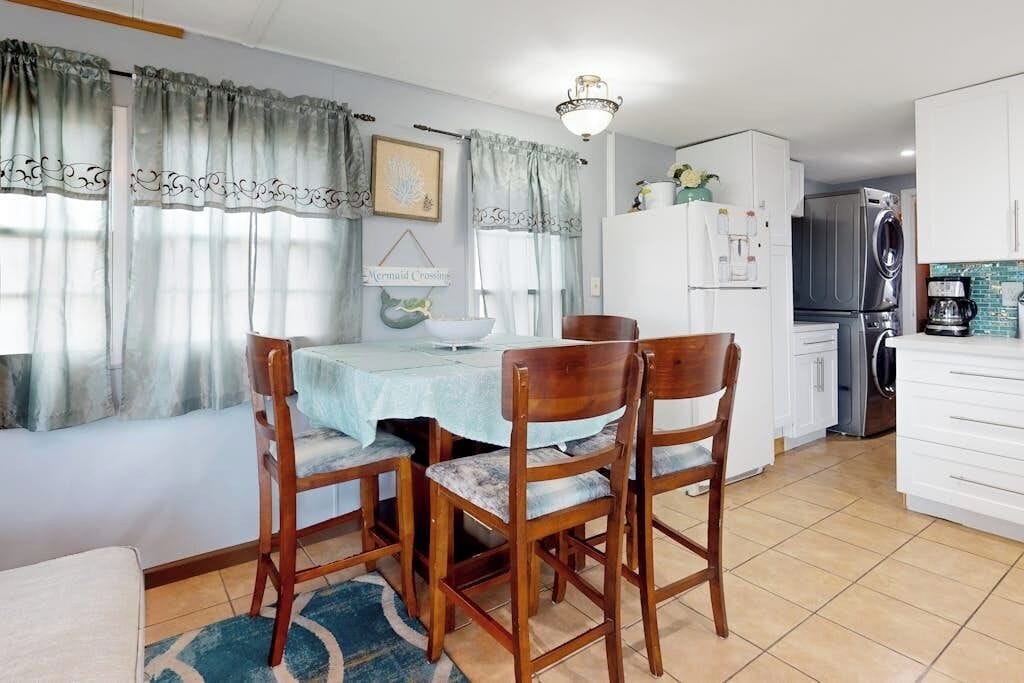 A dining area with a table and chairs, a refrigerator, and a coffee maker.