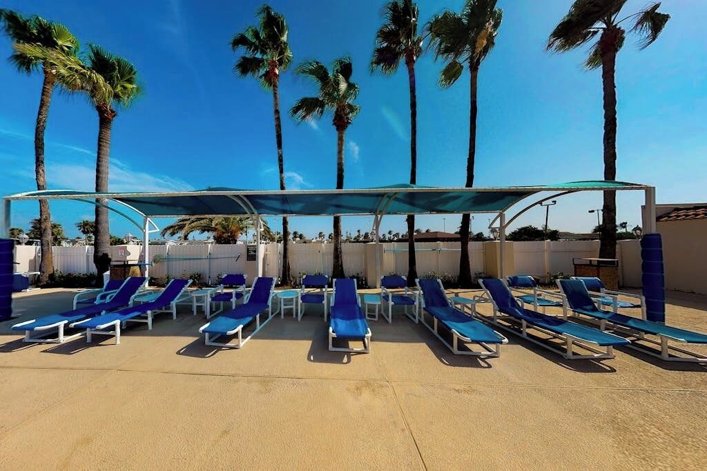 Un espace aménagé au bord de la piscine, avec des chaises longues et un coin salon abrité, le tout entouré de palmiers.