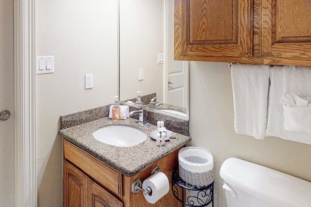 A bathroom with a granite countertop sink, wooden cabinets, a toilet, and a towel rack.