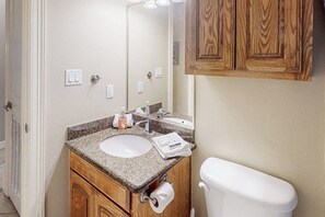 Ein Badezimmer mit einem weißen Waschbecken, einem Holz-Waschtisch, einem Spiegel und einer Toilette.