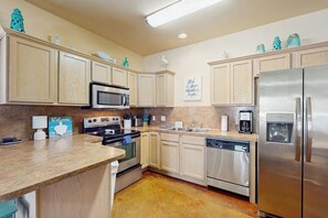 A kitchen with light-colored cabinets, stainless steel appliances, a coffee maker, and a water dispenser. - Palm Bay 408 - By The Pool Escape (Corpus Christi)
