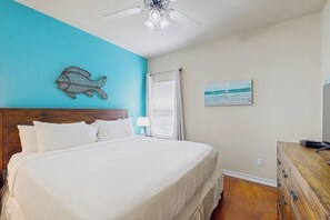 A bedroom with a bed, a ceiling fan, a wall-mounted fish decoration, a window with blinds, and a wooden dresser. - Palm Bay 408 - By The Pool Escape (Corpus Christi)