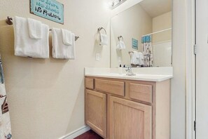 A bathroom with a white sink, wooden cabinets, a mirror, and a towel rack with white towels. - Palm Bay 408 - By The Pool Escape (Corpus Christi)