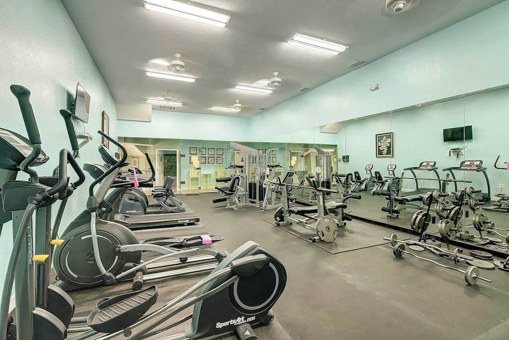 A gym with cardio machines, weightlifting equipment, and a large mirror.