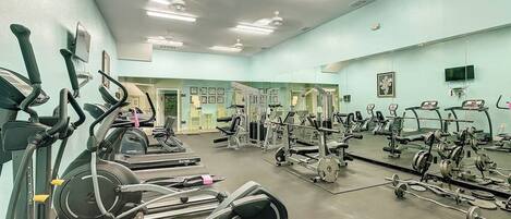 Et fitnesscenter med løbebånd, styrketræningsudstyr og et stort spejl.