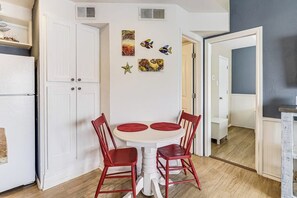 A compact kitchen with a dining area, white cabinetry, and a small table with red chairs. - Beach Club - Casa Del Sol (Corpus Christi)