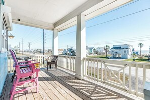 A wooden deck with a railing, two chairs, and a table. - Seahorse Beach House (Galveston)