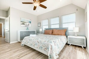 A bedroom with a bed, nightstands, a dresser, a ceiling fan, and a window with blinds. - Seahorse Beach House (Galveston)