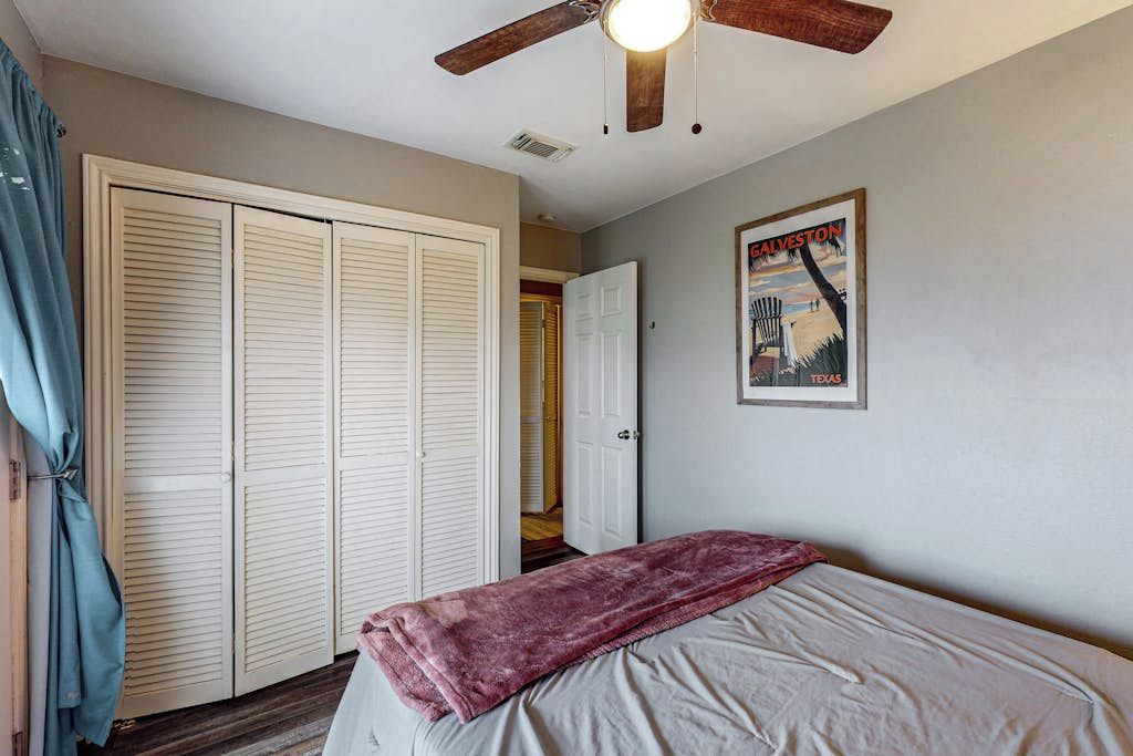 Ein Schlafzimmer mit einem Bett, einem Deckenventilator, einem Kleiderschrank und einer Tür zu einem anderen Raum.