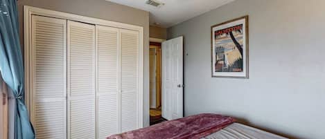 Un dormitorio con una cama, ventilador de techo, armario y una puerta que da a otra habitación.