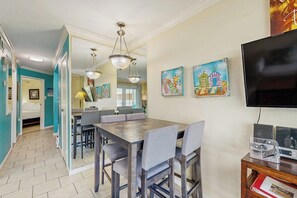 Un coin repas avec une table et des chaises en bois, un téléviseur posé sur un meuble et des œuvres d’art accrochées au mur.