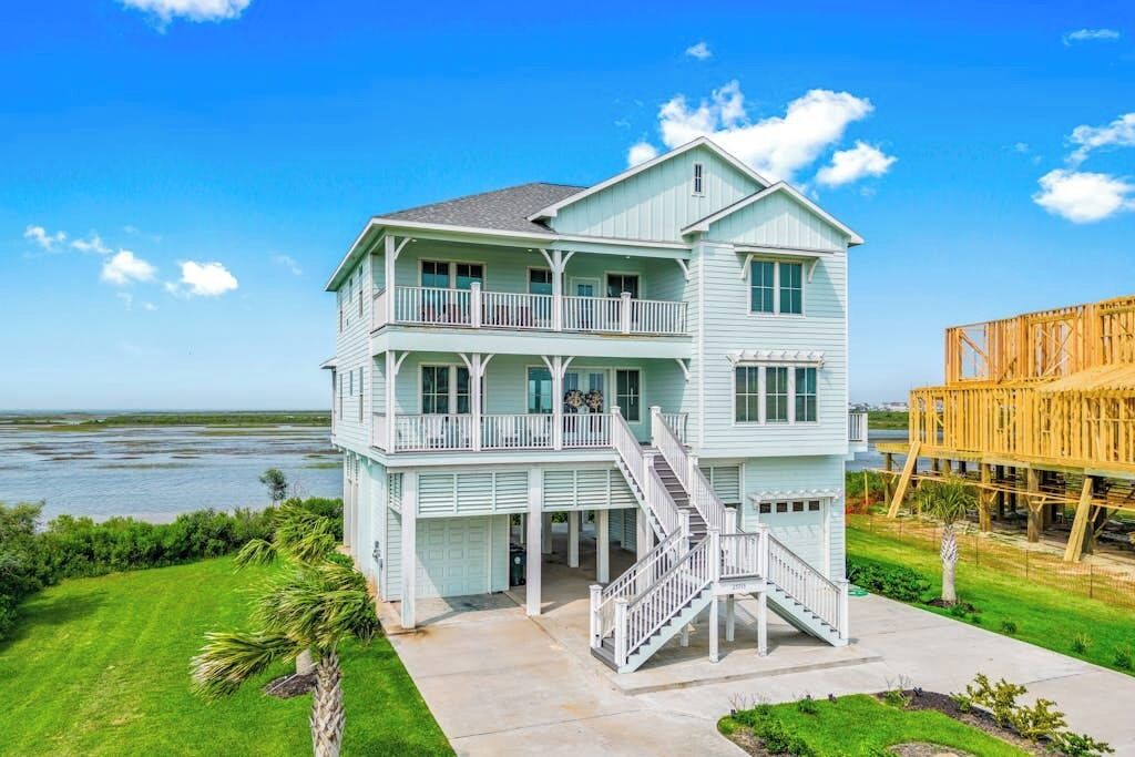 Une maison de deux étages située en bord de mer, dotée d’un balcon, d’un escalier et offrant une vue sur l’océan.