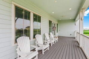 A covered porch with white Adirondack chairs and a view of the landscape. - Pointe West - Bay Breeze Paradise (Galveston)