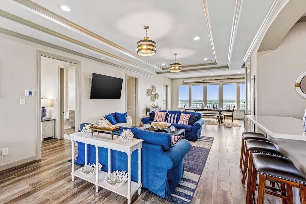 A spacious living room with a large window, a flat-screen TV mounted on the wall, and a dining area with a table and chairs.
