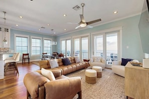 A spacious living area with a large sofa, ottomans, and a dining table. - Blue Claws - Bayfront, Elevator & Resort Pools (Galveston)