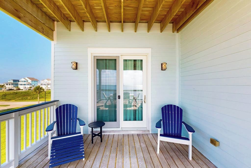 A covered porch with two Adirondack chairs, a small table, and a sliding glass door.