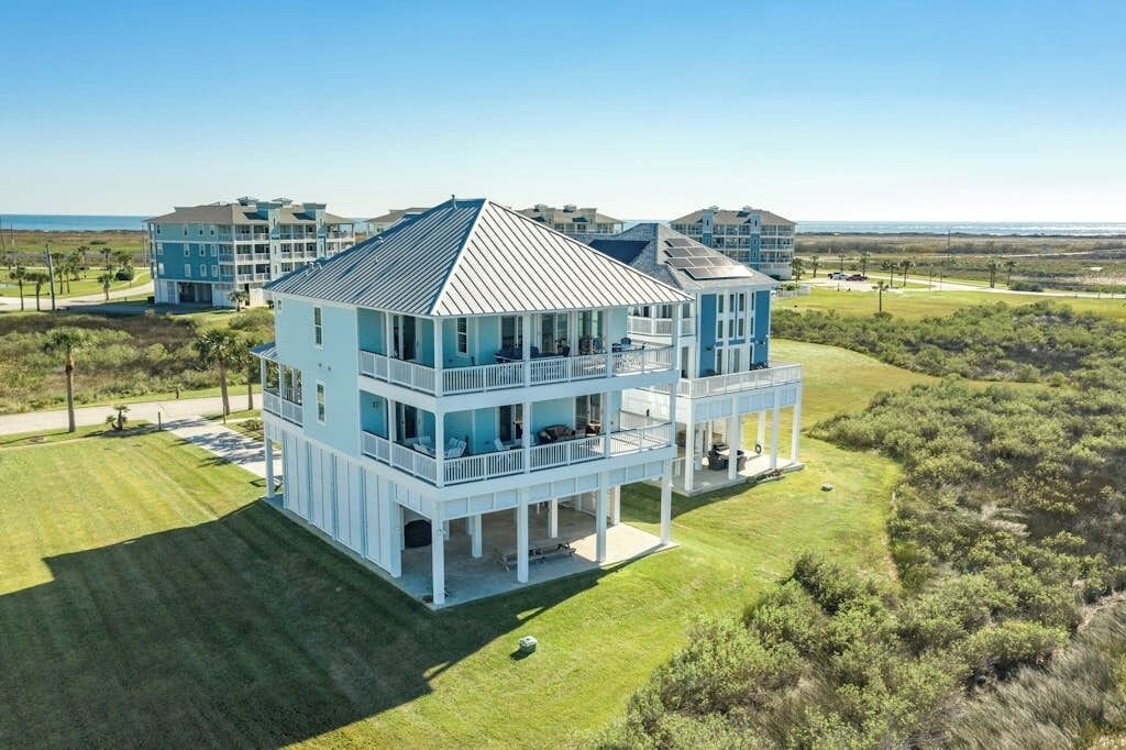 Une propriété en bord de mer, composée de plusieurs étages, dotée d’un balcon couvert et offrant une vue sur l’océan.