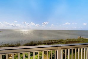 A view of a calm body of water with a wooden dock extending into it, surrounded by greenery. - Blue Claws - Bayfront, Elevator & Resort Pools (Galveston)