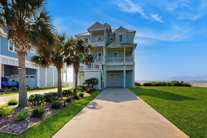A two-story residential building with a front entrance, a driveway, and a lawn with palm trees. - Blue Claws - Bayfront, Elevator & Resort Pools (Galveston)