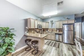 A modern kitchen with a central island, stainless steel appliances, and a light blue wall. - Palm Bay 504 - Heated Pool & Dog-Friendly (Corpus Christi)