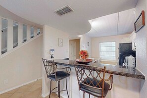A kitchen with a central island, bar stools, a refrigerator, and a window with blinds. - Aztec Habitat No 19 - Pool, 1 Minute to the Beach (South Padre Island)