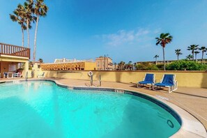 Ein Swimmingpool mit Liegestühlen, Palmen und einem Gebäude im Hintergrund.