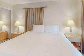 A hotel room with a large bed, two bedside tables with lamps, a mirror, and a curtain. - Aztec Habitat No 19 - Pool, 1 Minute to the Beach (South Padre Island)