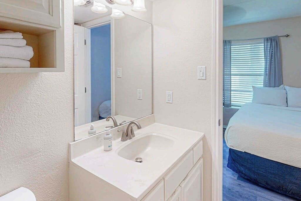 A hotel room with a white sink, mirror, and a bed with blue bedding.