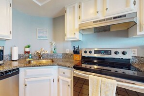 A kitchen with white cabinets, a granite countertop, a stainless steel stove, and a wall-mounted microwave. - Inverness #304 - Steps to Beach, Pool & Hot Tub (South Padre Island)