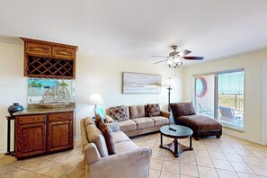 A living room with a sofa, armchair, coffee table, wooden cabinet, and a ceiling fan. - Suntide II Condominiums #106 (South Padre Island)