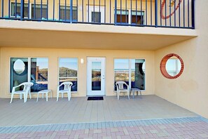 A building with a balcony, white plastic chairs, and a door with glass panels. - Suntide II Condominiums #106 (South Padre Island)