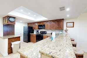 A kitchen with wooden cabinets, a granite countertop, a built-in oven, and a microwave. - Suntide II Condominiums #106 (South Padre Island)